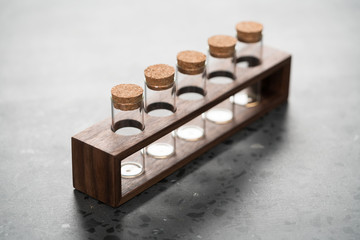 walnut holder with glass tubes for spices on concrete surface
