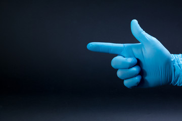 A gun sign by right man hand in a blue medical glove on a black background