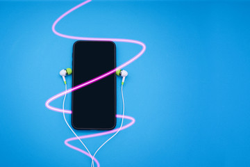 Fototapeta premium Hand phone equipped with earphones on blue background.