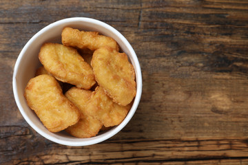 Bucket with tasty chicken nuggets on wooden table, top view. Space for text
