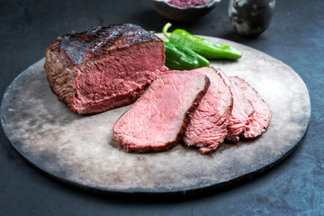 Traditioneller Rostbraten vom Rind aufgeschnitten mit Chili und Rotem Salz als closeup auf einem rustikalen Modern Design Teller