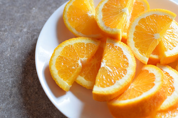 Fototapeta na wymiar Juicy sliced of orange on white round plate on grey grunge table background with copyspace. Healthy snack.