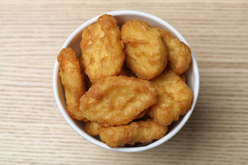 Bucket with tasty chicken nuggets on wooden table, top view