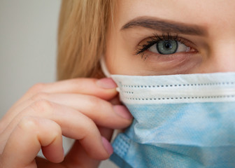 Beautiful Women In A Medical Mask. Blond young woman wearing medical mask adjusting it with her hands close up