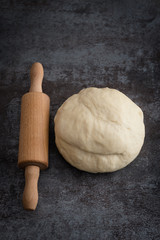 Freshly knead the dough and rolling pin on a dark background. Top view