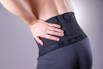 Man with a medical belt for the back on a gray background