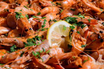 Close up of large portion of cooked shrimps with tomato sauce and yellow lemons in a large pan at a street food festival, ready to eat healthy seafood, beautiful orange monochrome outdoor background