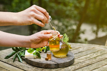 Concept of natural organic oil in cosmetology. Moisturizing skin care and aromatherapy.  Laboratory test outdoor, woman doing reserch and dropping extract from pipette. Wooden background, copy space 