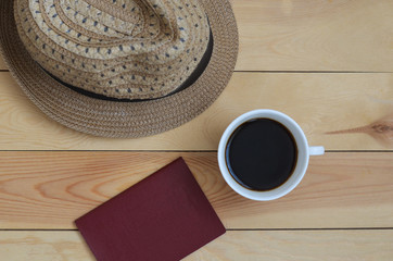 A cup of coffee, a straw hat and a passport on a wooden table top view. The concept of vacation and travel