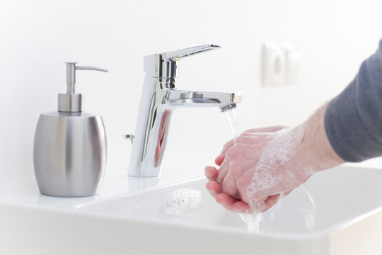 Man washing his hands with liquid soap in a white bathroom to protect himself against infection