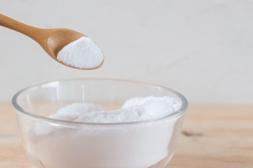 Baking soda in glass bowl and spoon on wooden background