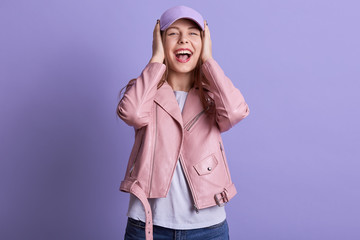 Picture of beautiful charming sweet female opening mouth widely, laughing, being in high spirits, covering her ears with both hands, no hearing, wearing casual clothes. People and emotions concept.