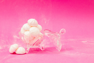 Meringues in a glass bowl on a pink background