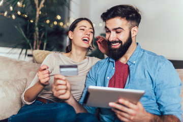 Smiling couple using digital tablet and credit card at home