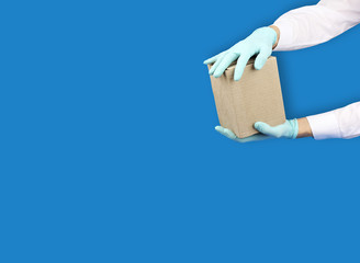 two hands in blue medical gloves holds cardboard box, courier delivery in virus quarantine, copy space blue background