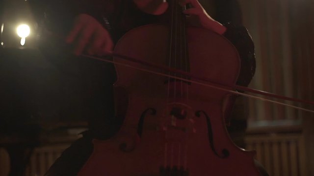 Close up shot of female cello player hands playing cello in concert room with red lightning. Cello bow.