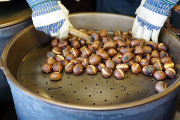 male hands stirring and roasting delicious organic chestnuts on a gas barrel stove with wooden ladle