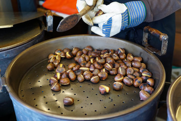 male hands stirring and roasting delicious organic chestnuts on a gas barrel stove with wooden ladle
