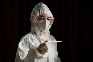 Woman wearing gloves with biohazard protective suit and mask. With unhappy face, hand holds...