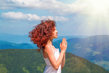 Young beautiful woman praying in the mountain with blue sky and white clouds.