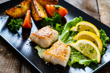Fish dish - fried cod fillet with vegetables on wooden table