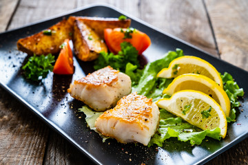 Fish dish - fried cod fillet with vegetables on wooden table