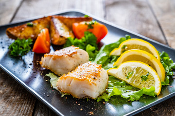 Fish dish - fried cod fillet with vegetables on wooden table