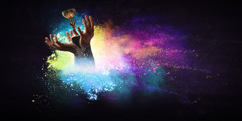 Hands holding champion cup on colourful splashes background. Mixed media
