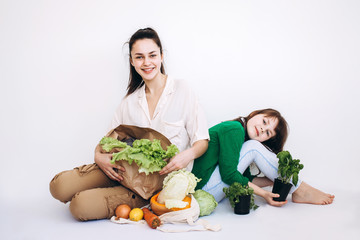 Smiling Girls with a paper eco bag of healthy vegetables and greens, isolated on white. Healthy eating concept. Zero waste concept. Eco friendly natural bag with organic fruits and vegetables.