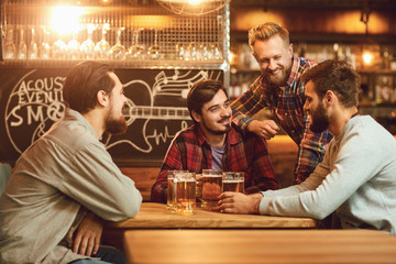 A group of friends is sitting in a bar with glasses of beer. - obrazy, fototapety, plakaty