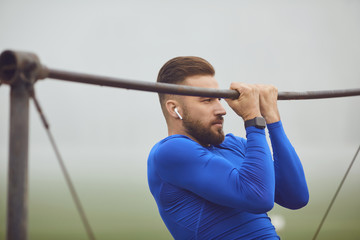 A bearded guy doing pull-ups on a horizontal bar in a stadium in the fog.