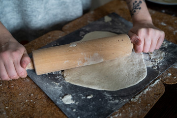 Fototapeta Kobieta robi ciasto na naleśniki. Wałkuje ciasto z mąką na drewnianym stole obraz