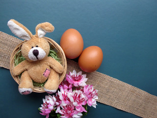 Easter holiday flat lay. Fluffy toy rabbit in a nest with flowers and eggs on a green background. Copy space for your text