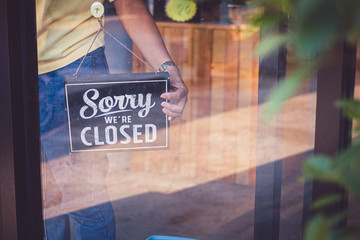 Woman Holding up a shop sign saying: Sorry we're Closed