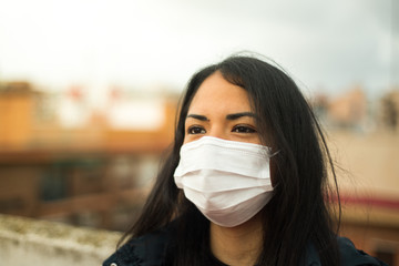 Young latin girl with pollution mask looking at the horizon, urban background in the city