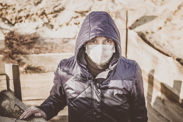 Woman in a disposable medical mask near a wooden fence. Coronavirus epidemic. A man in a medical mask stands in a trench. Covid 19. Pandemic. Quarantine.