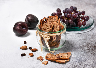 Slices of dry rusk fruit bread in a glass jar with fresh plums and grapes. Homemade healthy food concept. Selective focus. 