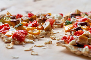 Tasty traditional Tarte Flambee from the Alsace region of France with a thin pastry crust topped with creme fraiche or cheese, onions, herbs, lardons and tomato sliced ready to serve as an appetizer