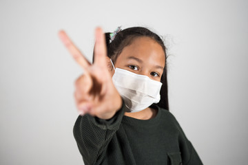 Lttle girl with medical mask show v sign with hand, healthcare and infection control. Concept of positivism against the infection of the coronavirus, quarantine kids.