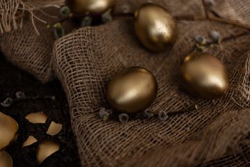 Golden easter eggs are scattered on a dark background with dry green branches. eggs in a golden bowl.