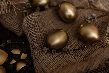 Foto op Plexiglas Golden easter eggs are scattered on a dark background with dry green branches. eggs in a golden bowl. © mavrik