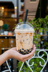 woman is holding a plastic cup of bubble milk tea