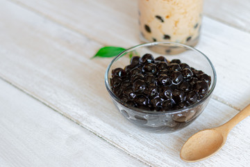 A glass cup of pearl milk tea and a plate of tapioca ball on wooden background.