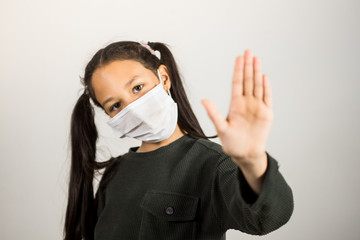 Cute latin girl with protective mask, makes the stop gesture with his hand on a white background, focus on the hand.
