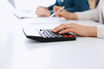 Accountant checking financial statement or counting by calculator income for tax form, hands closeup. Business woman sitting and working with colleague at the desk in office. Tax and Audit concept