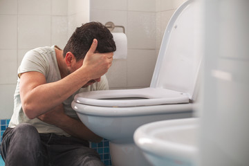 Man feeling bad putting his head in toillet and vomiting. - obrazy, fototapety, plakaty