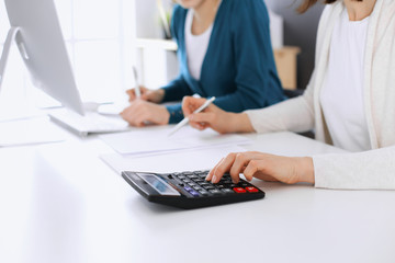 Accountant checking financial statement or counting by calculator income for tax form, hands closeup. Business woman sitting and working with colleague at the desk in office. Tax and Audit concept