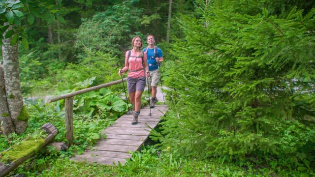 Man and woman passing over small bridge with Trekking equipment. Topla Valley, Crna na Koroskem, Slovenia.