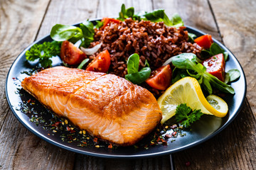 Fried salmon steak with red rice and vegetables on wooden table