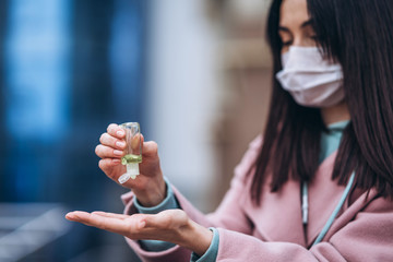 Fototapeta premium Close up hands of female in medical mask cleaning her hands with sanitizer outdoor in the city to prevent virus deseases. Coronavirus, COVID-19, epidemic, pandemic, quarantine concept.